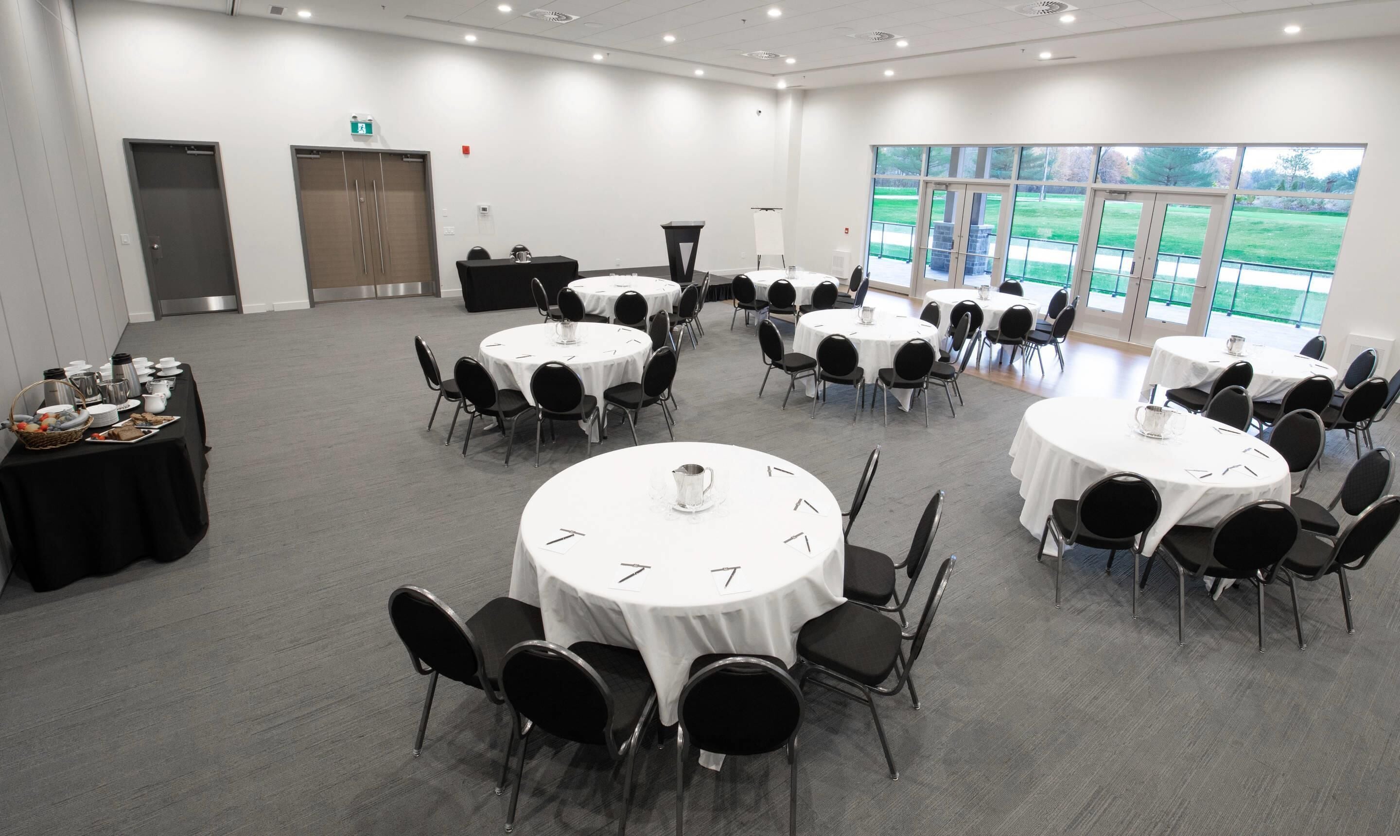 Une salle de conférence équipée de plusieurs tables rondes, de chaises et d’un buffet proposant des plats et des boissons.