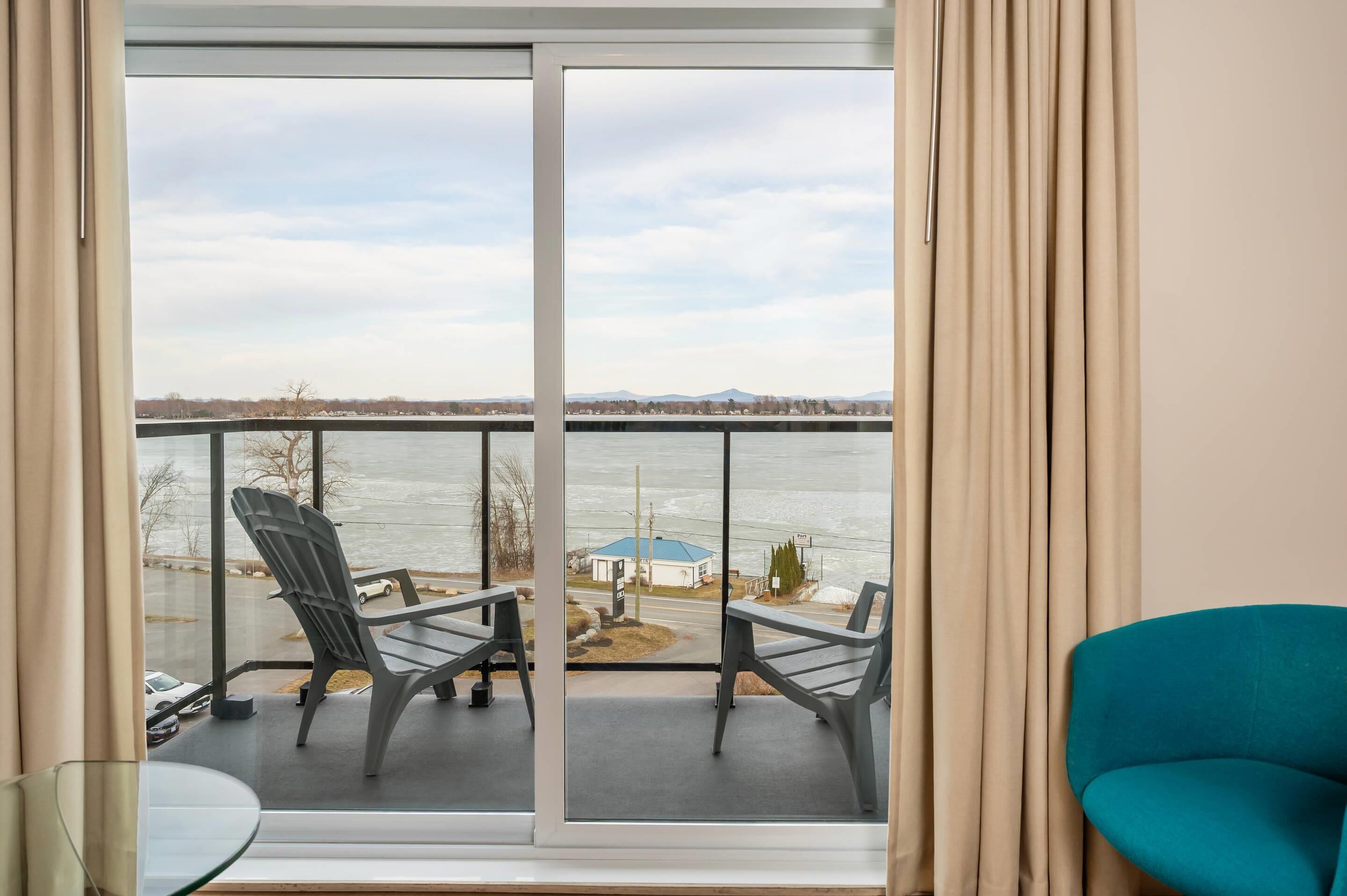 Ein Balkon mit Blick auf ein Gewässer und eine entfernte Landschaft, mit zwei Stühlen und einem Tisch.