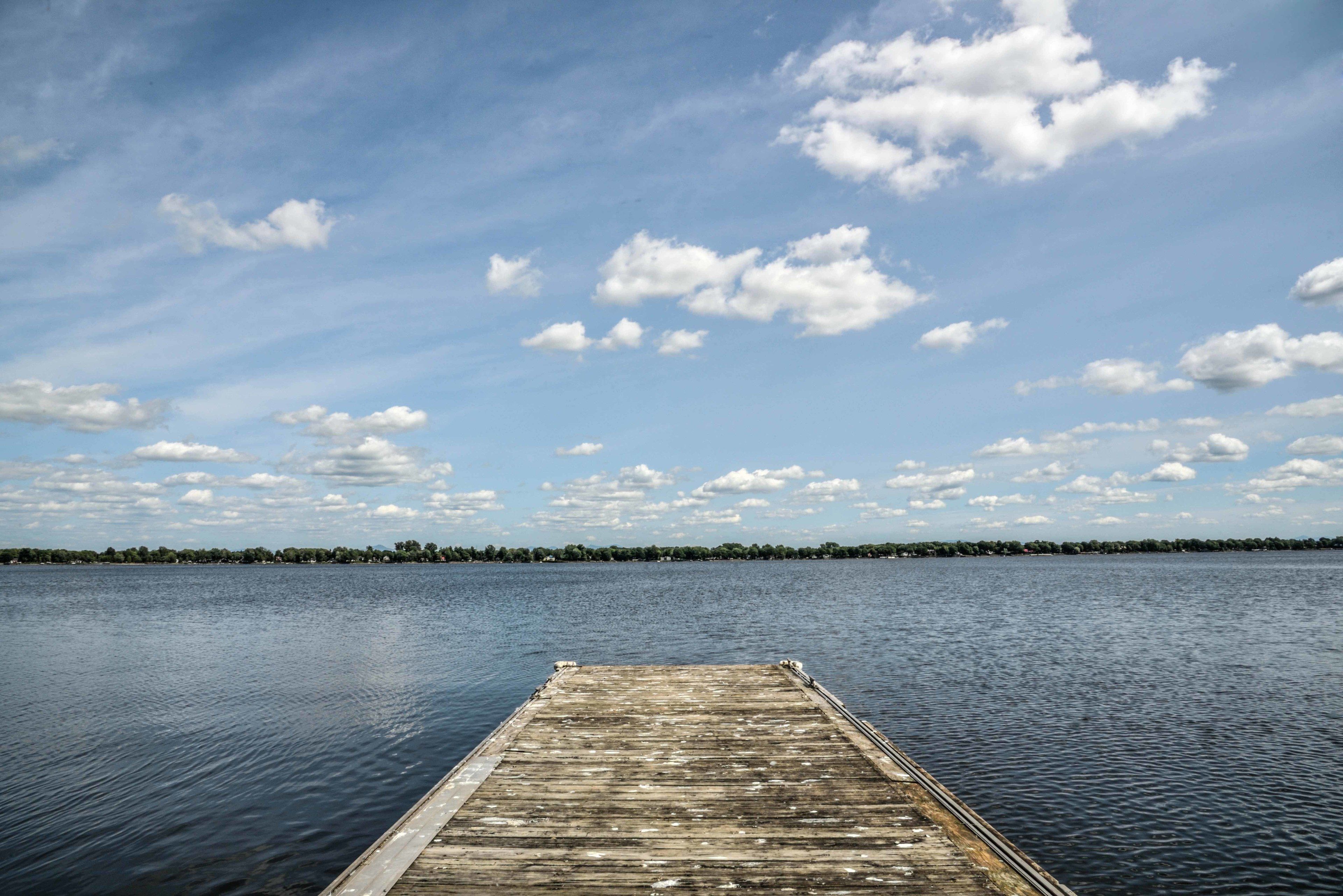 A wooden pier extending into calm water with a clear sky and distant shoreline.