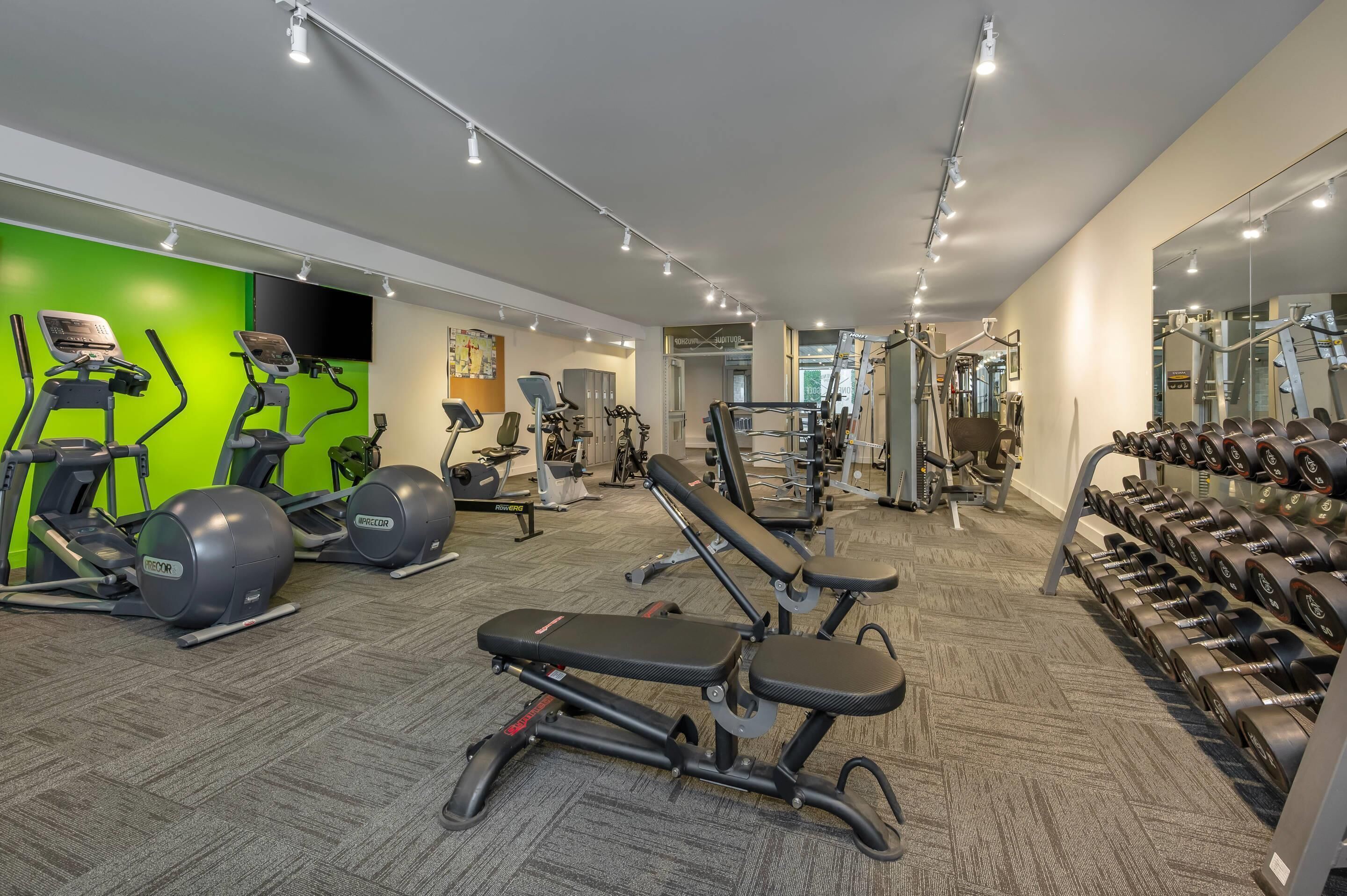 Une salle de sport équipée de divers appareils d’exercice, notamment des tapis de course, des vélos elliptiques et des poids libres.