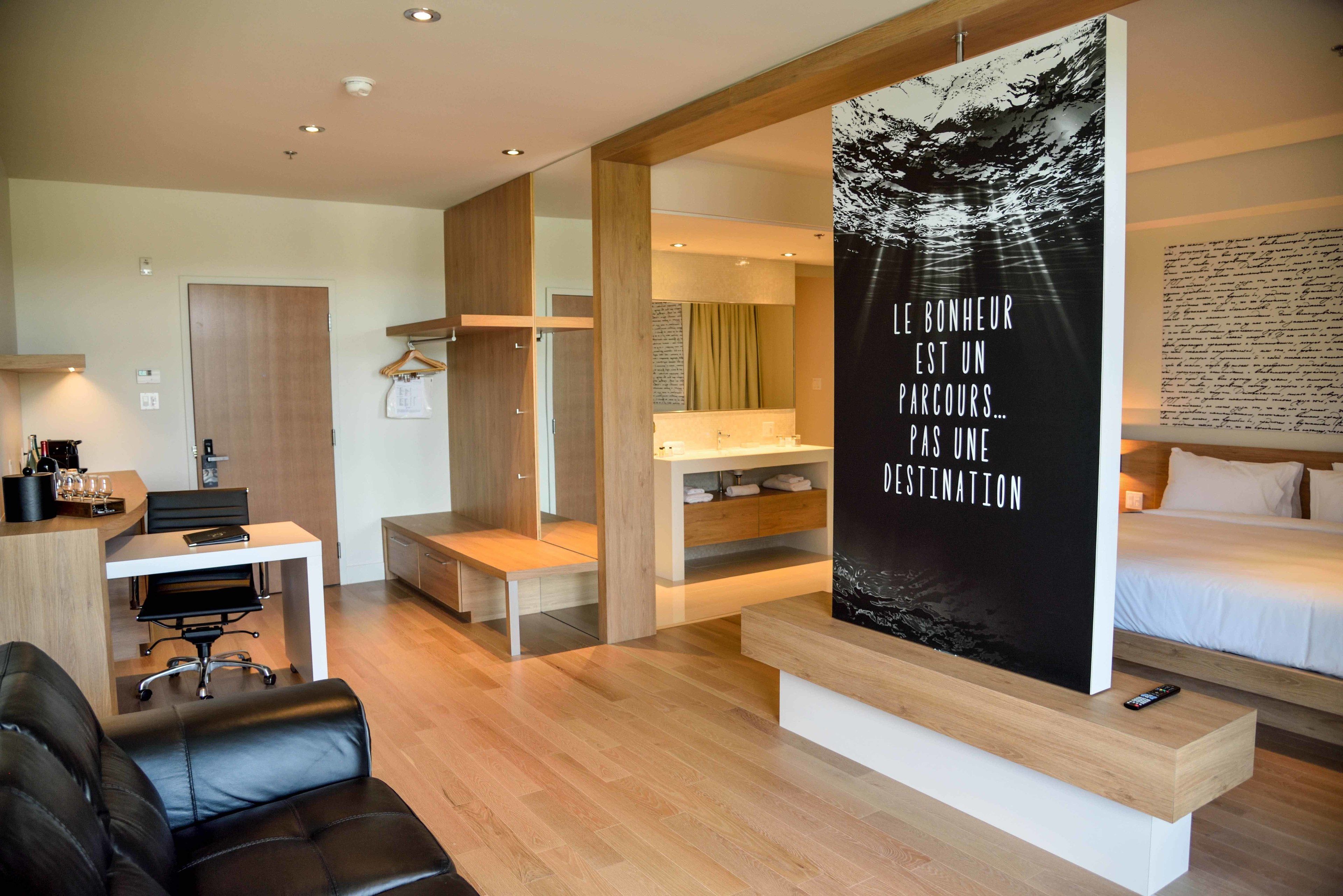 Una habitación de hotel moderna con un escritorio de madera, un sofá de cuero negro, una cama y un cartel grande en la pared.