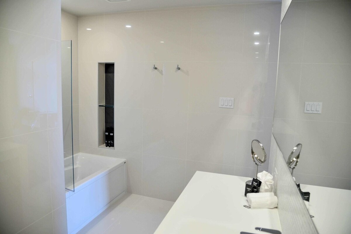 Un baño moderno con cabina de ducha de vidrio, bañera blanca y tocador con espejo y toalla.