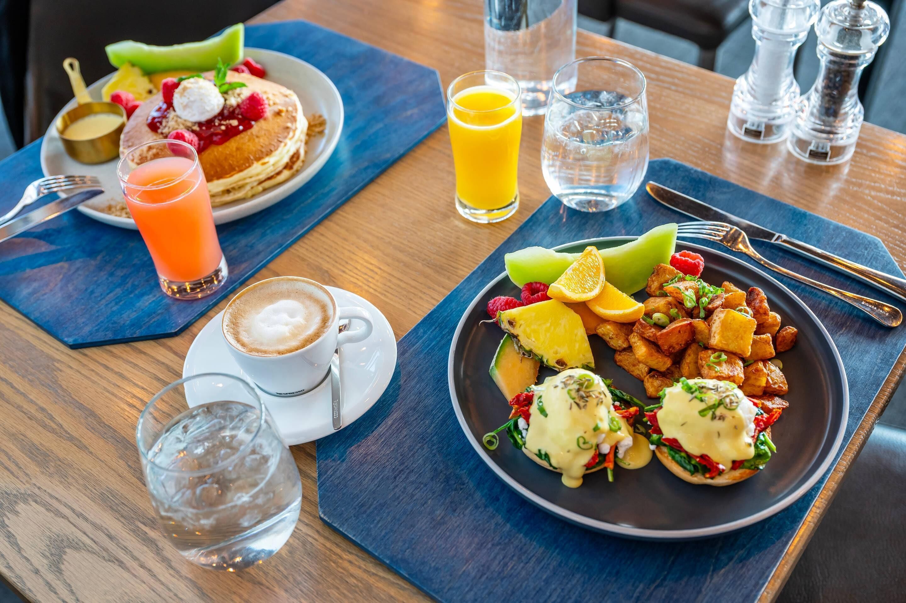 A breakfast setting with pancakes, fruit, and coffee on a wooden table.