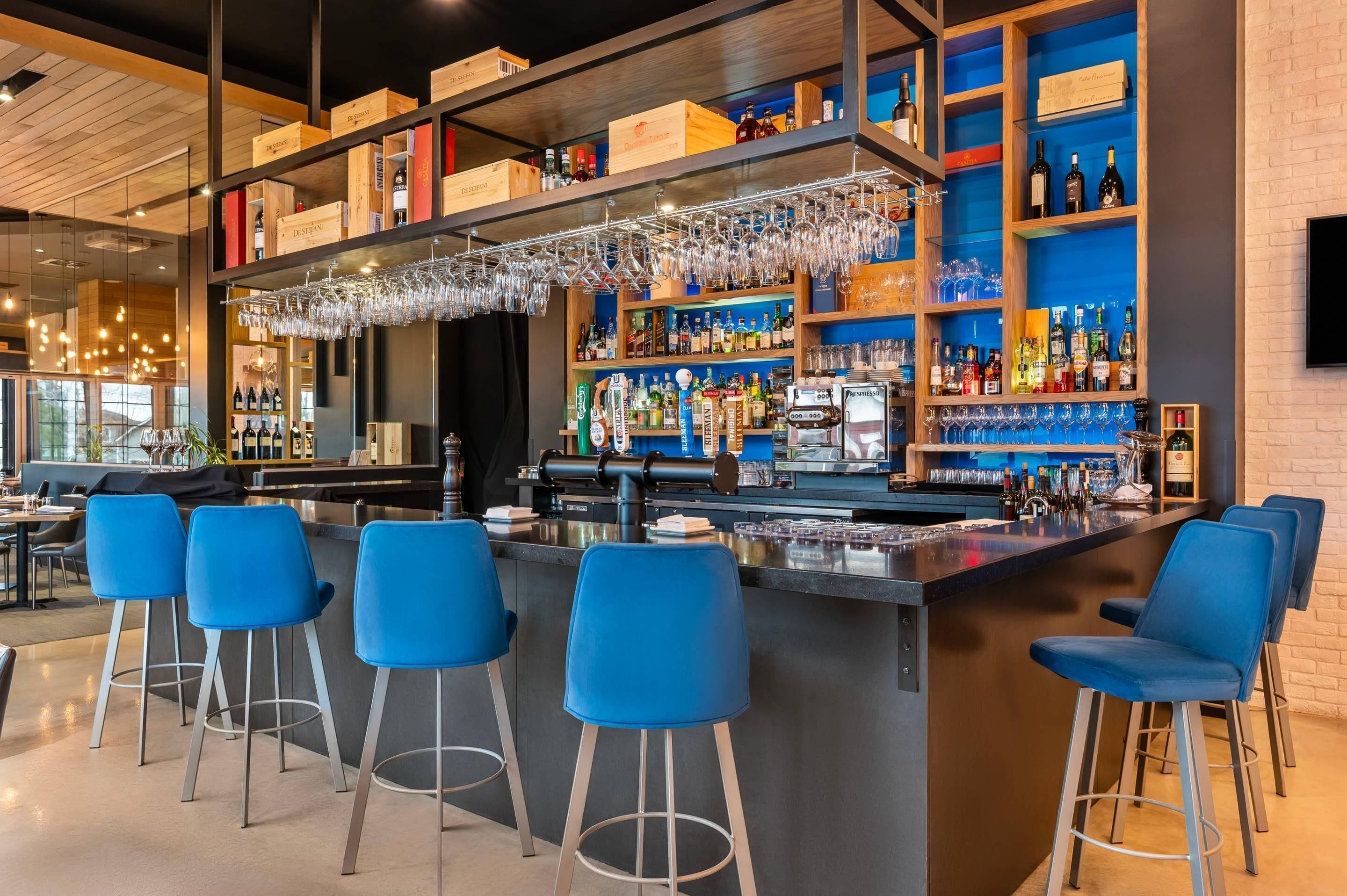 A bar area with a bar counter, stools, and shelves stocked with bottles.
