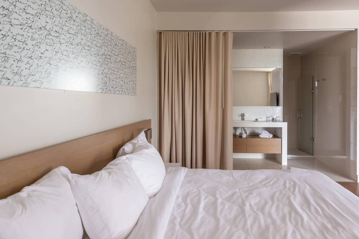 A hotel room with a bed, a bathroom with a shower, and a mirror.