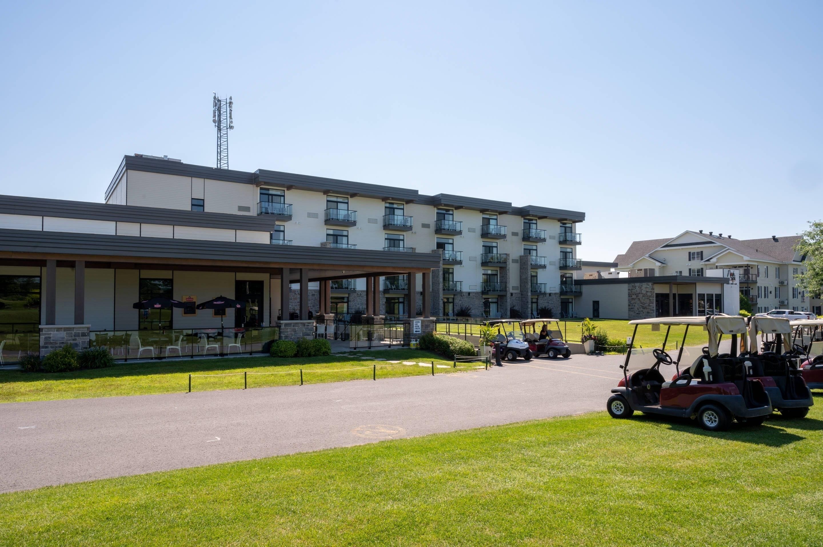 Un hotel de varios pisos con un espacio exterior cubierto, estacionamiento y carritos de golf.
