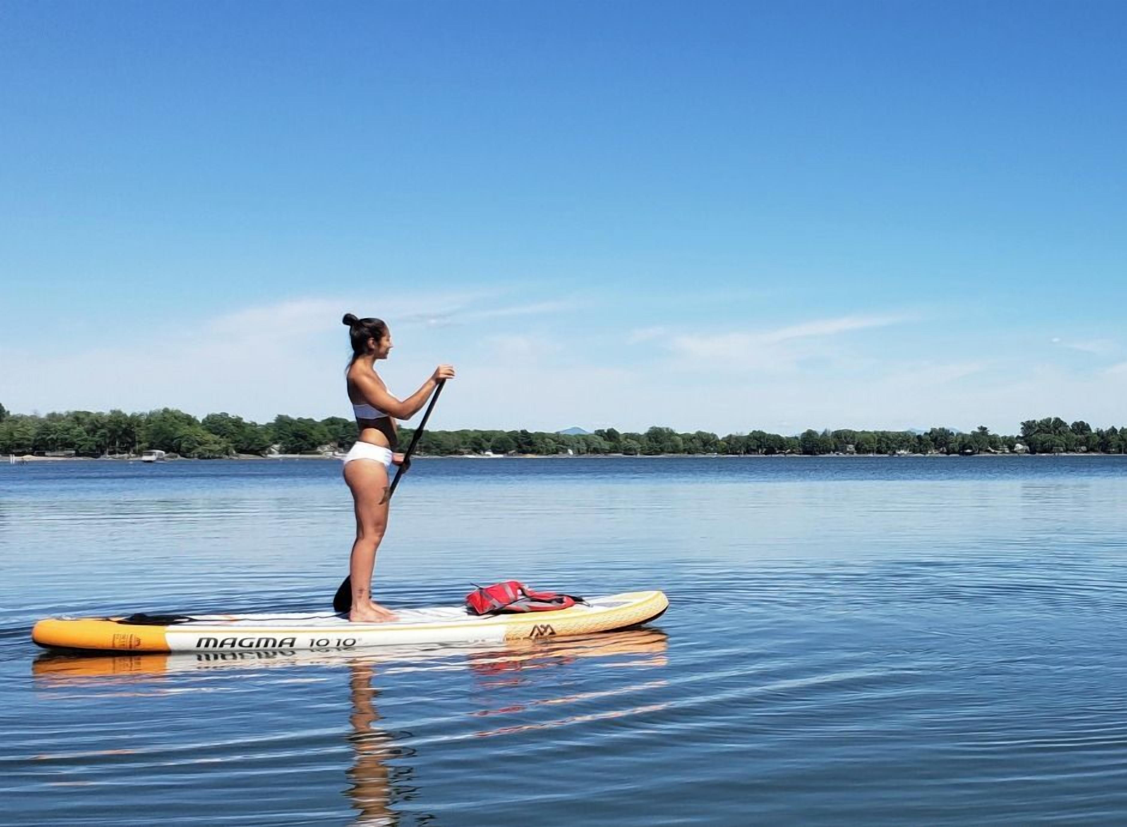 Una persona practicando paddleboard en un lago tranquilo con cielo despejado.