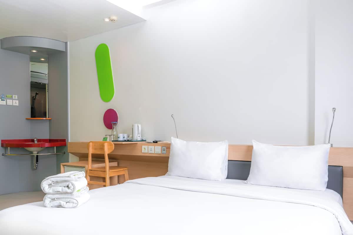 Une chambre d’hôtel avec un lit, un bureau et une chaise, un lavabo rouge et un miroir.