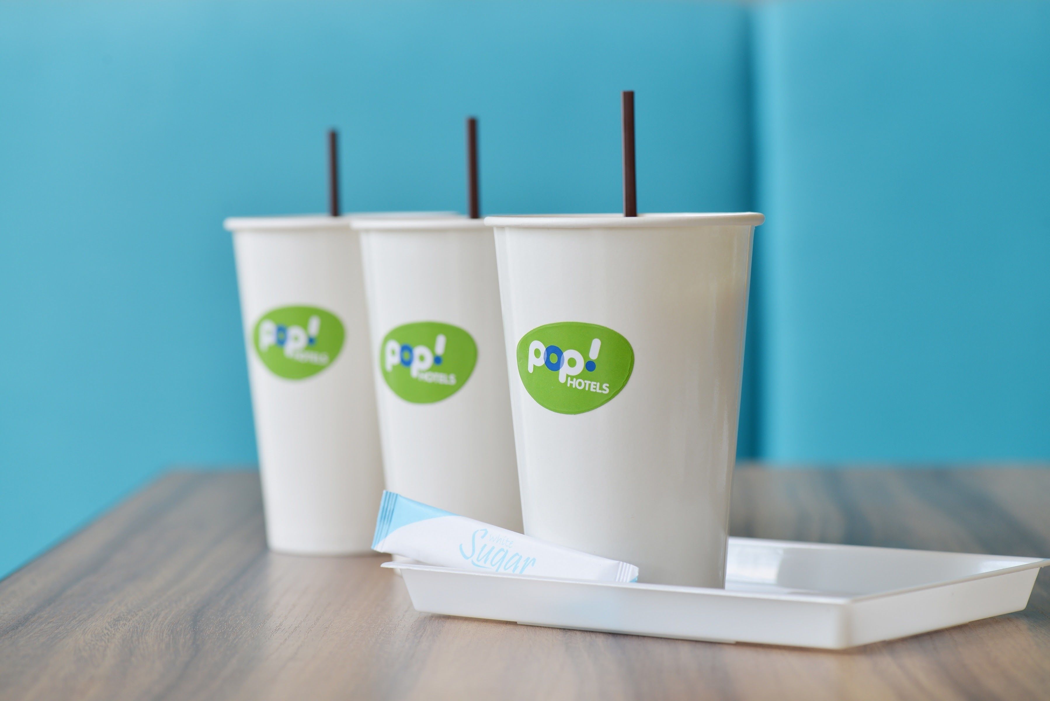 Drei Papierbecher mit 'pop! hotels'-Branding und eine Ablagefläche mit einem Servietten-Etikett mit der Aufschrift 'Zucker'.
