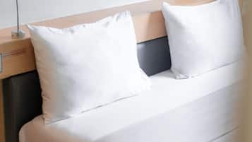 Una cama bien hecha con ropa de cama y almohadas blancas, un cabecero de madera y una mesita de noche con una lámpara.