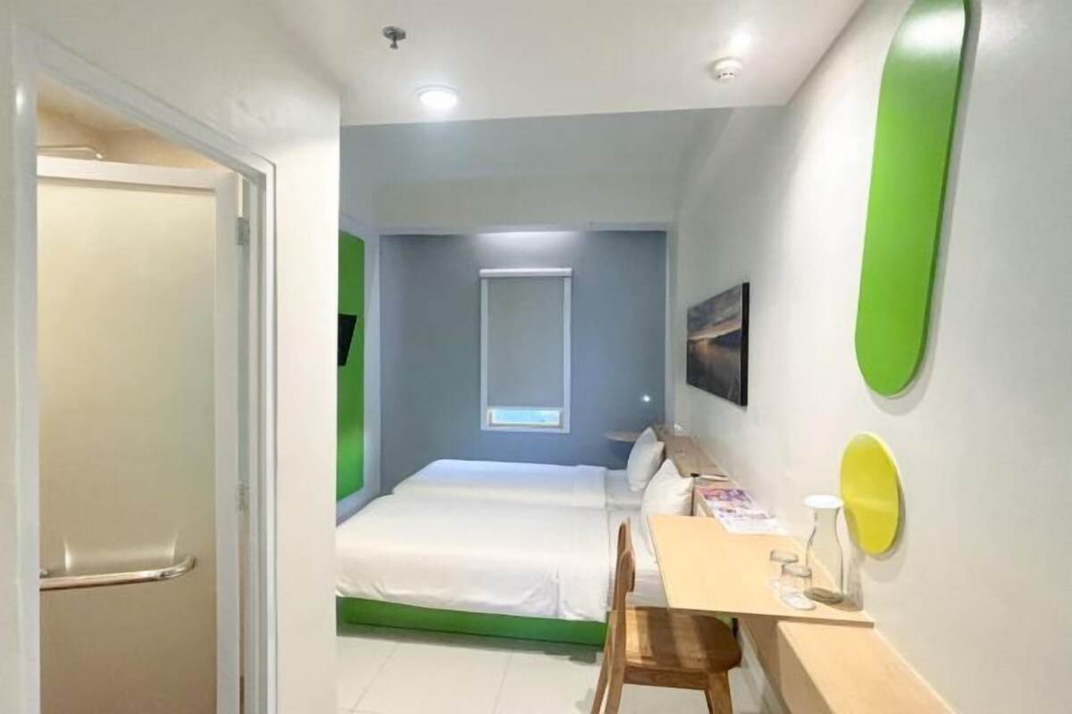 Une chambre d’hôtel avec un lit, un bureau et une chaise. Il y a une fenêtre donnant sur l’extérieur.