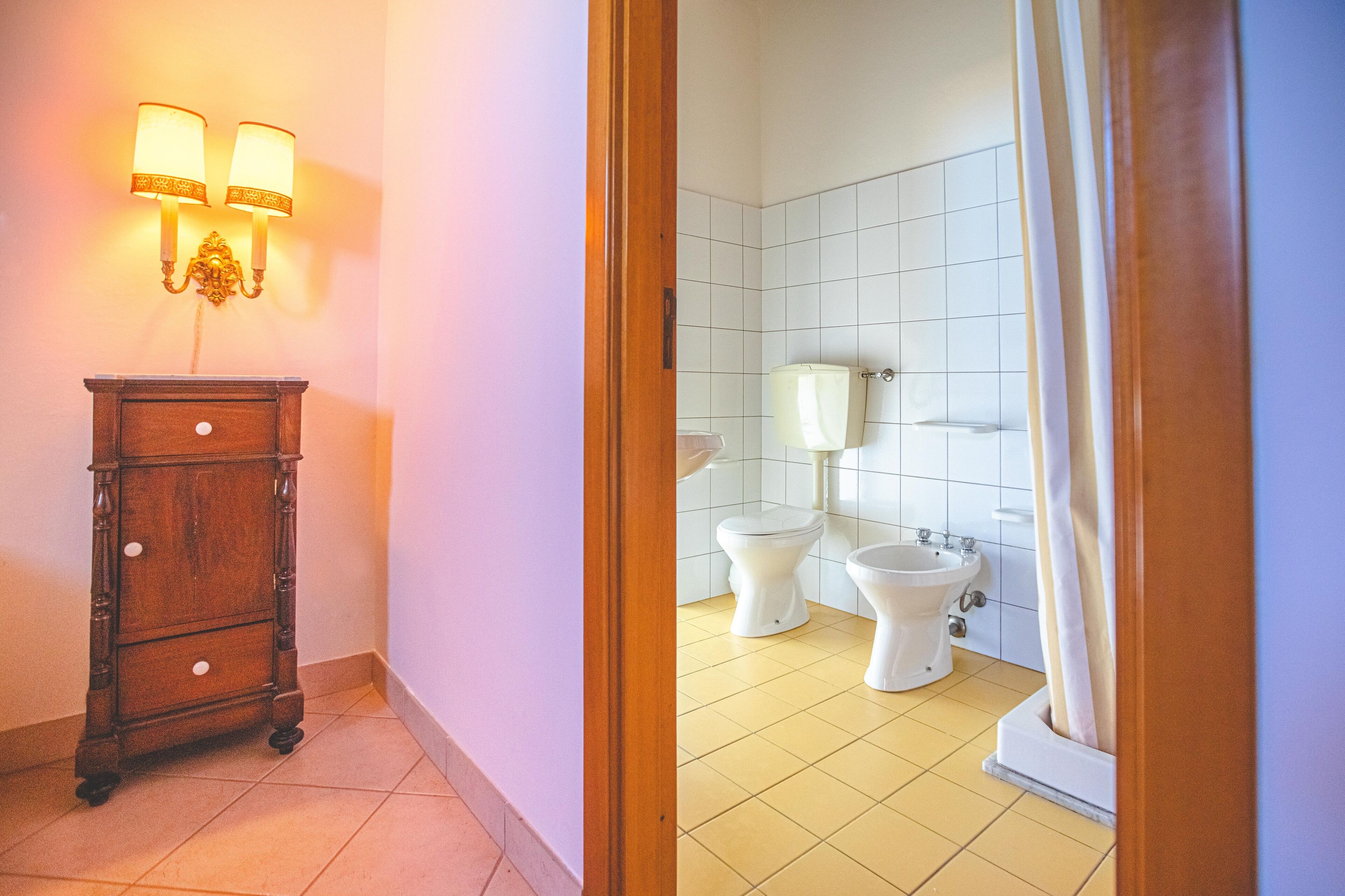 Une salle de bain avec deux toilettes, un bidet et un meuble en bois doté d’un luminaire.