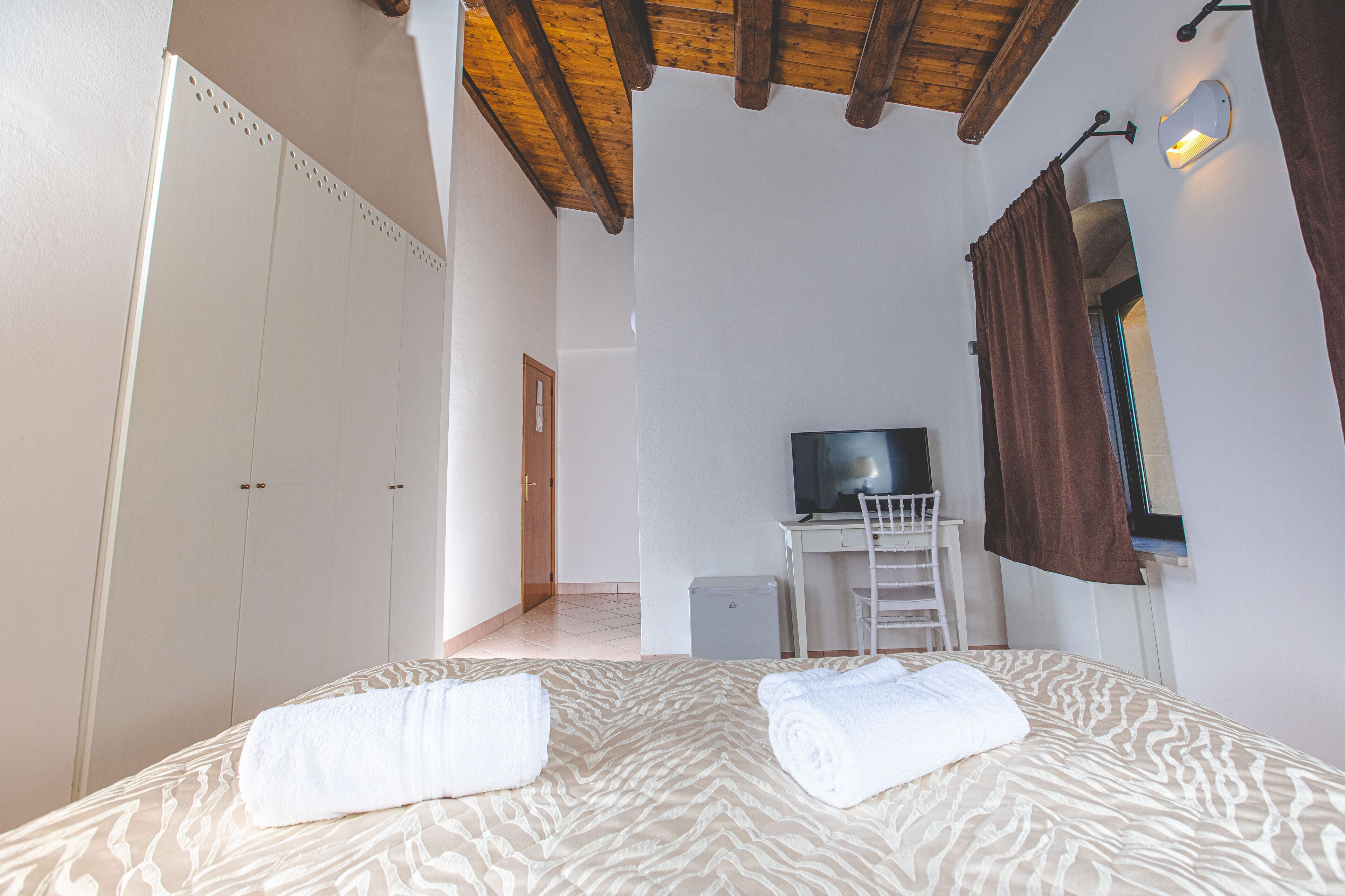 A bedroom with a bed, a desk with a chair, a television, and a wardrobe.
