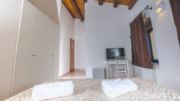 A bedroom with a bed, a desk with a chair, a television, and a wardrobe.