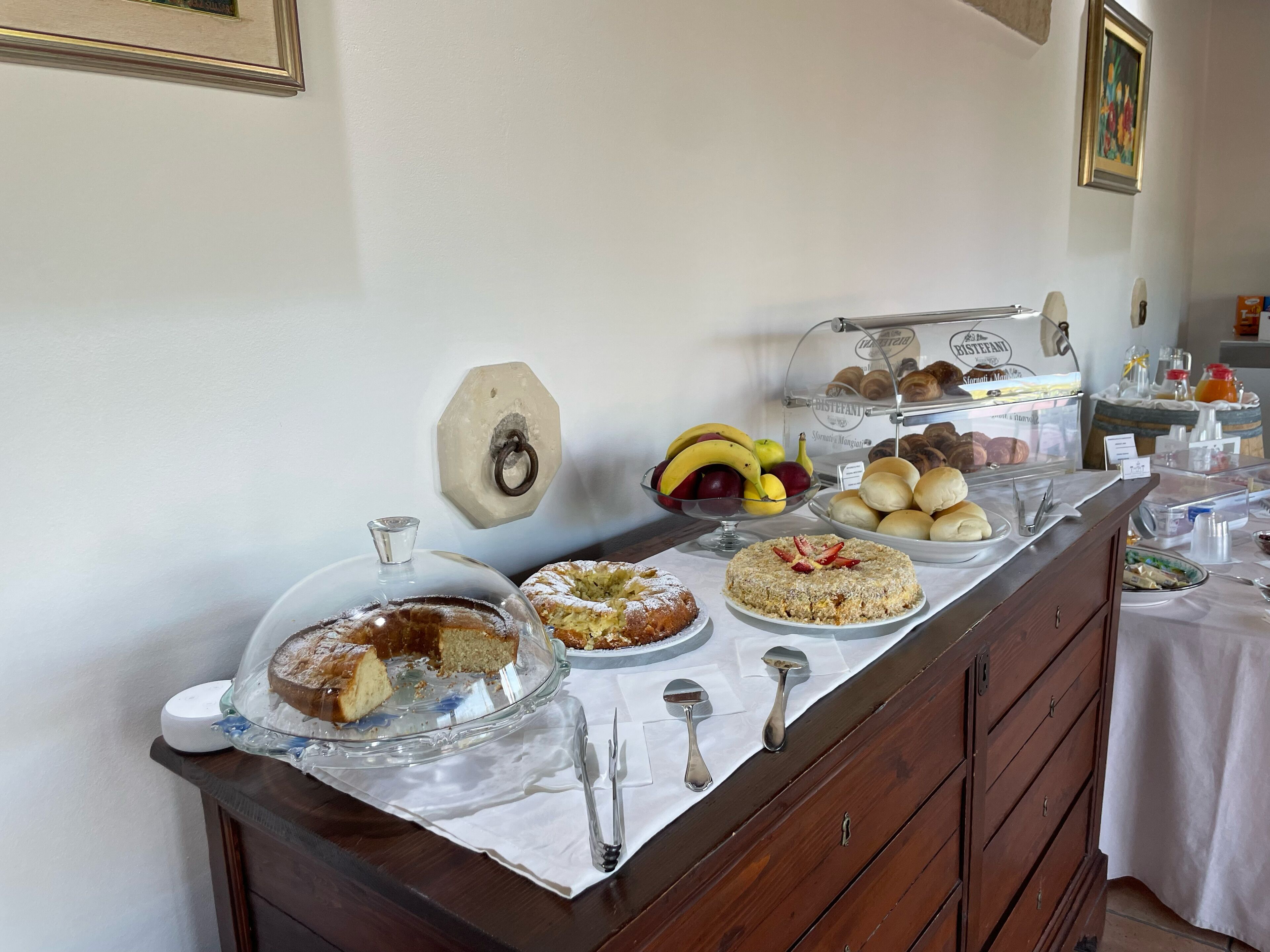 A buffet with various food items, including fruits, pastries, and a cake, displayed on a table with a white tablecloth.