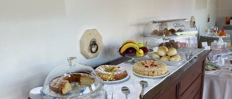 A buffet with various food items, including fruits, pastries, and a cake, displayed on a table with a white tablecloth.