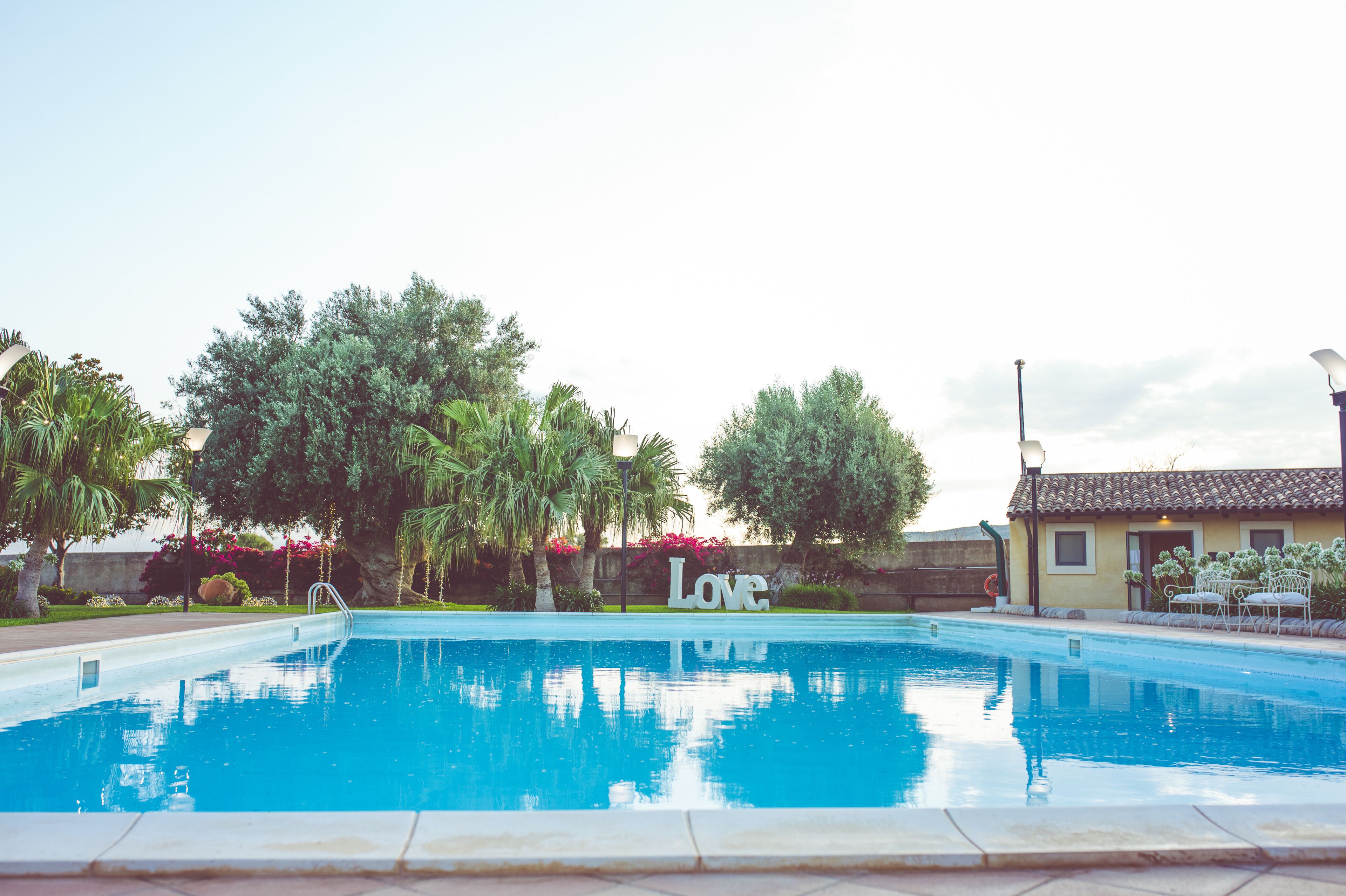 A swimming pool with a 'Love' sign, surrounded by greenery and a building with a tiled roof.
