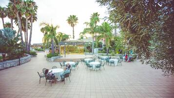 An outdoor patio area with round tables and chairs, surrounded by palm trees and a gazebo.