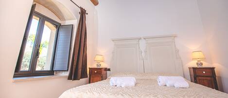 A bedroom with a large bed, two bedside tables with lamps, a window with curtains, and a wooden ceiling.