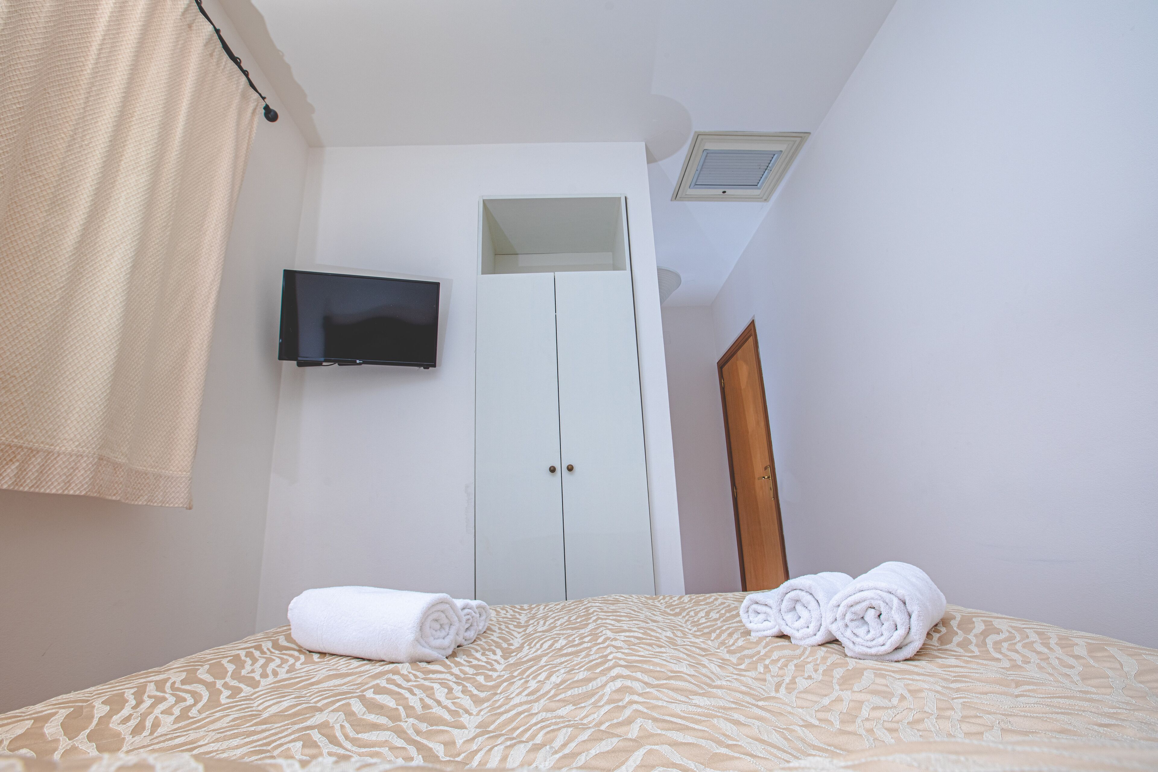 A hotel room with a bed, a TV mounted on the wall, a wardrobe, and a mirror.