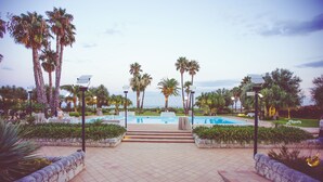 Zona de piscina con escalones que bajan al agua, rodeada de palmeras y muros de piedra.