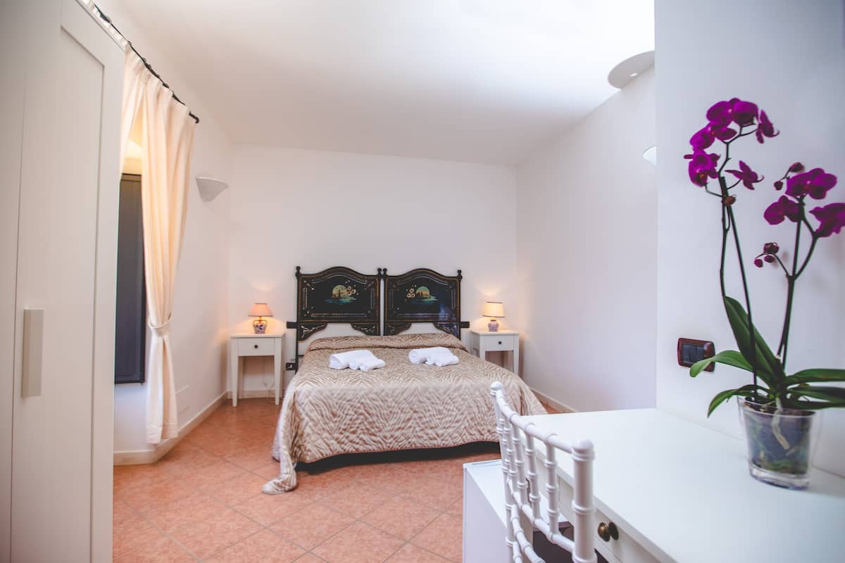 Une chambre à coucher avec un lit, des tables de chevet, une chaise, une plante en pot et un rideau.