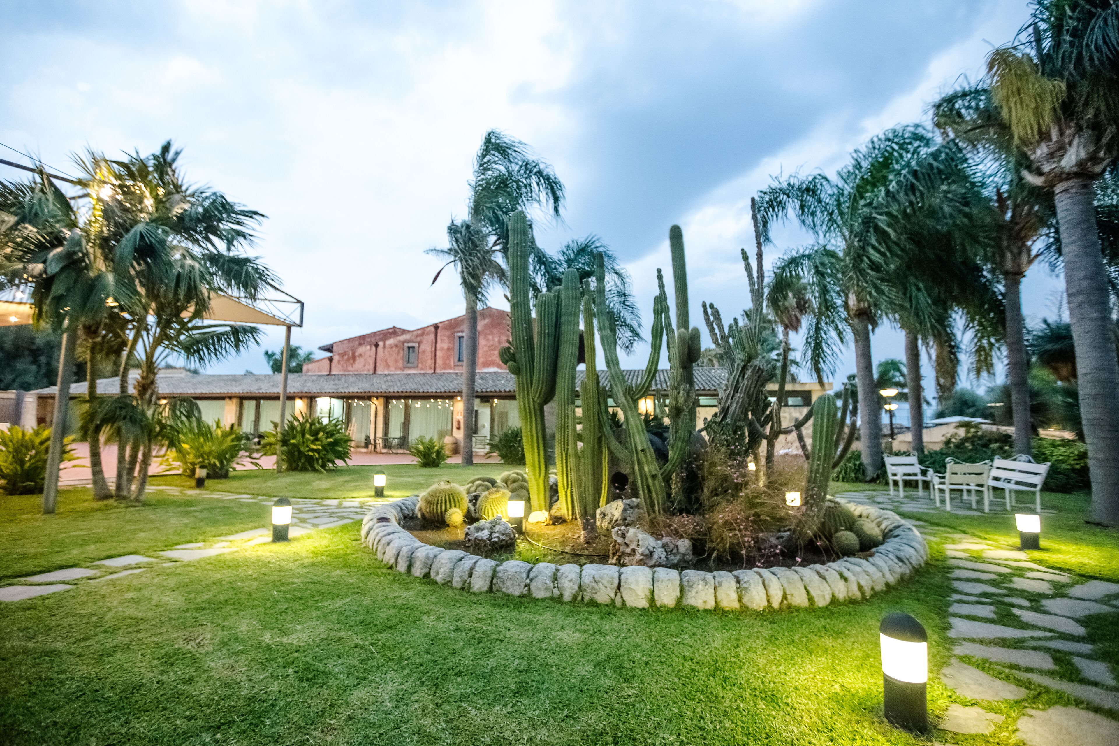 Um jardim bem cuidado, com cactos e palmeiras, caminhos de pedra e áreas de estar ao ar livre.