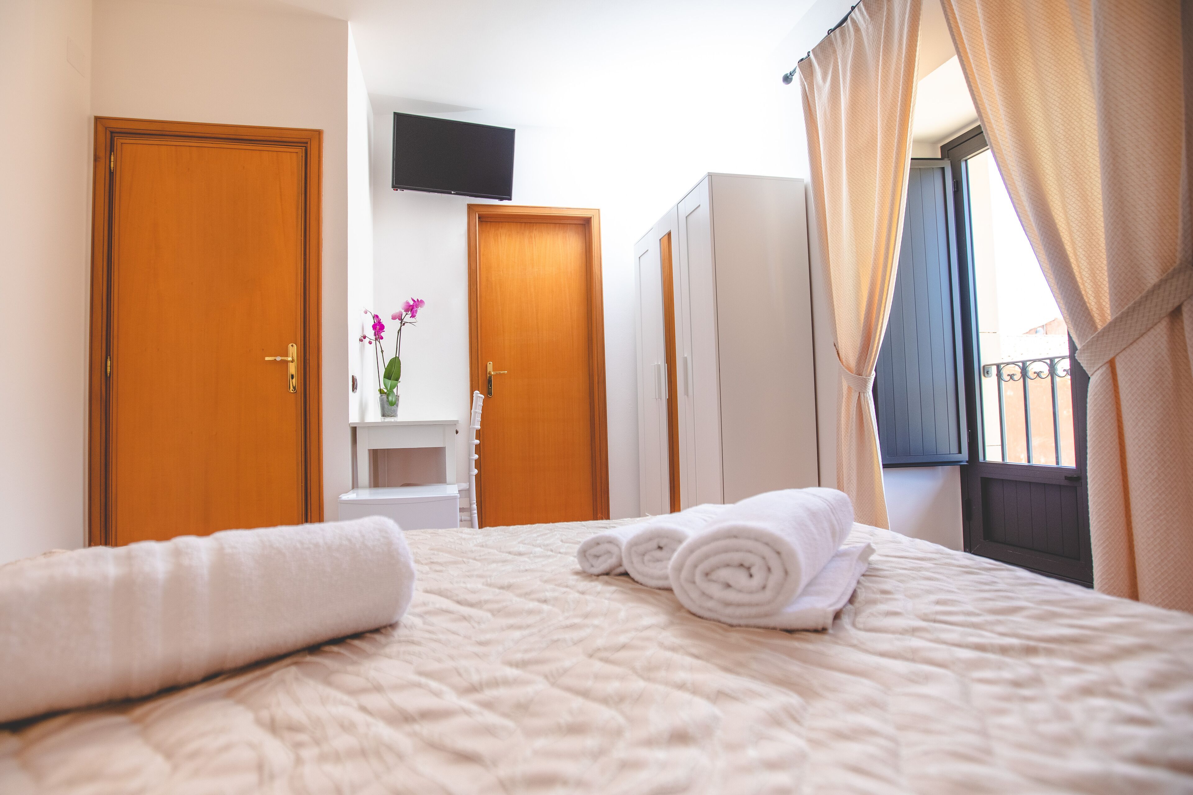 A hotel room with a bed, a TV mounted on the wall, and a window with curtains.