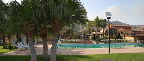 A pool area with palm trees, a clear sky, and a building in the background.