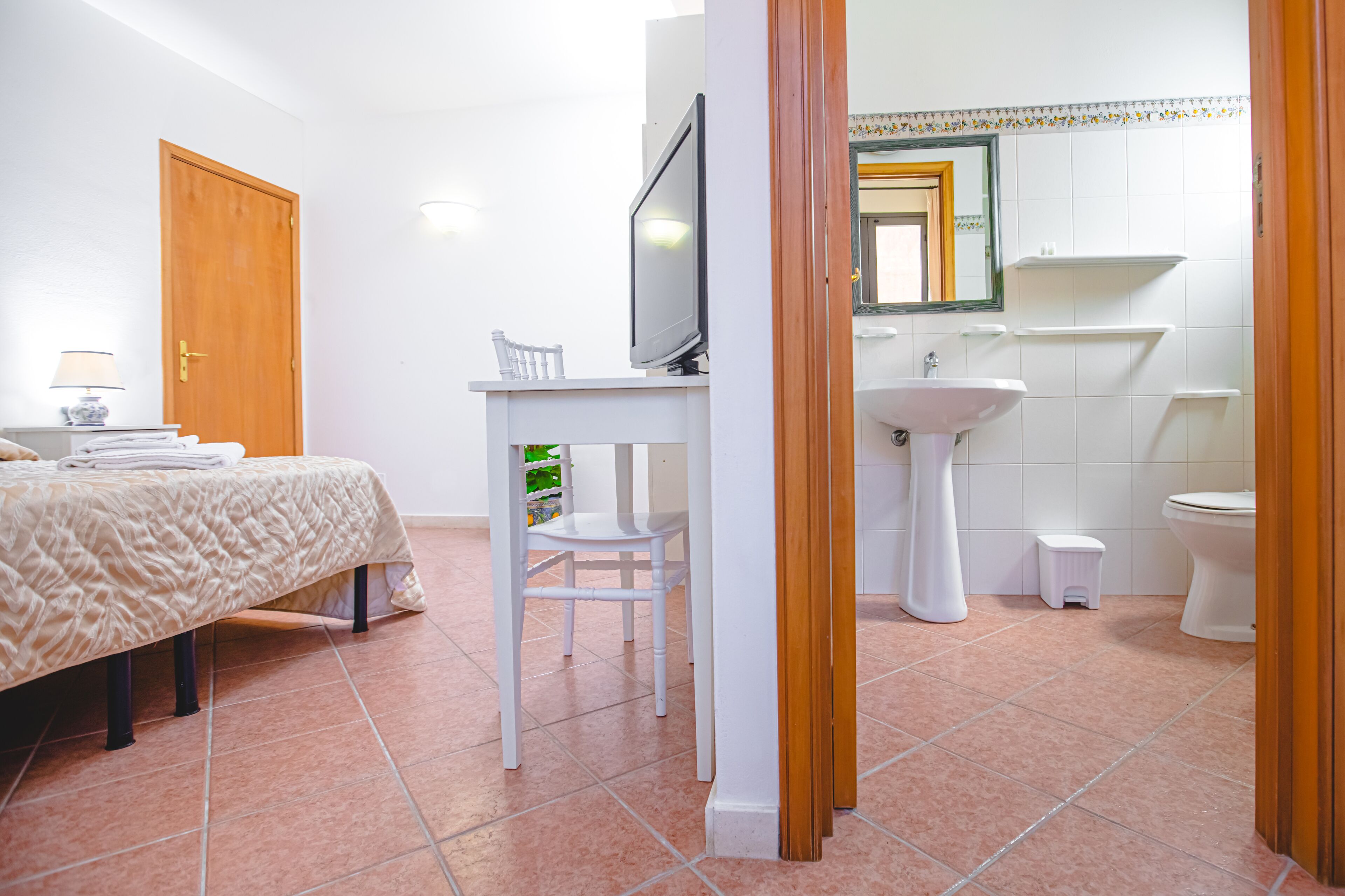 Une chambre à coucher comprenant un lit, un bureau, une chaise, un téléviseur et une salle de bain avec un lavabo et des toilettes.