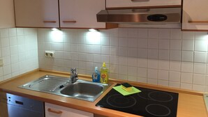 A kitchen with white cabinets, a stainless steel sink, a dishwasher, and a black stove. - Ferienwohnung Zacharias (Bad Hersfeld)