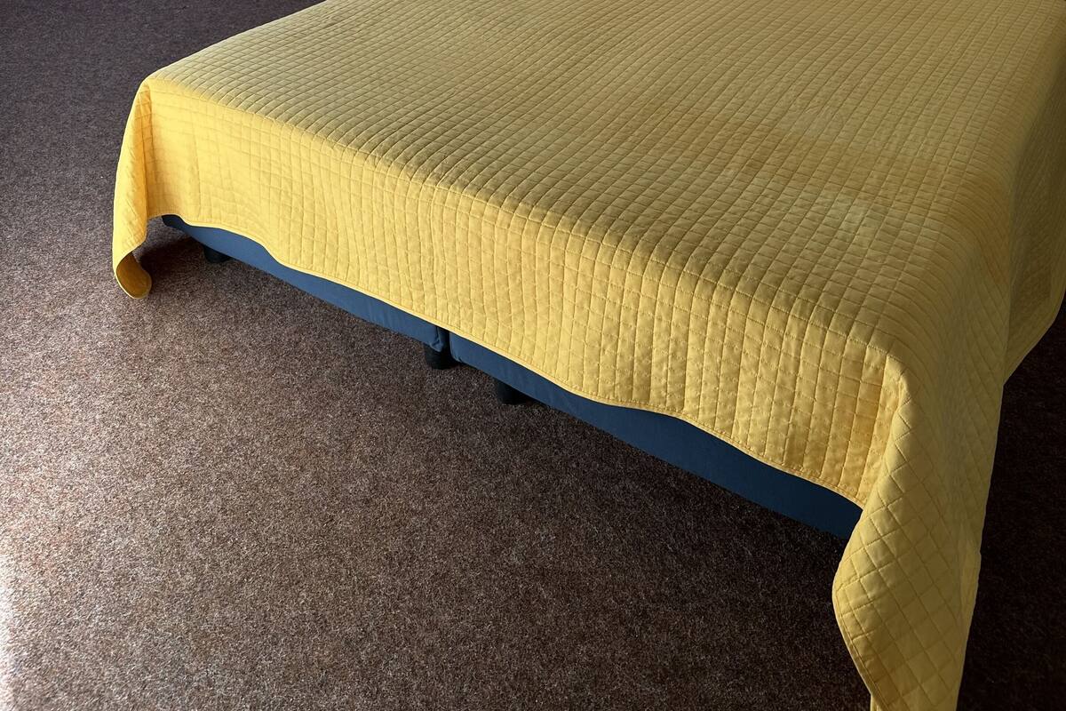 Une chambre à coucher avec un lit, une lucarne, des armoires en bois et un petit tabouret.