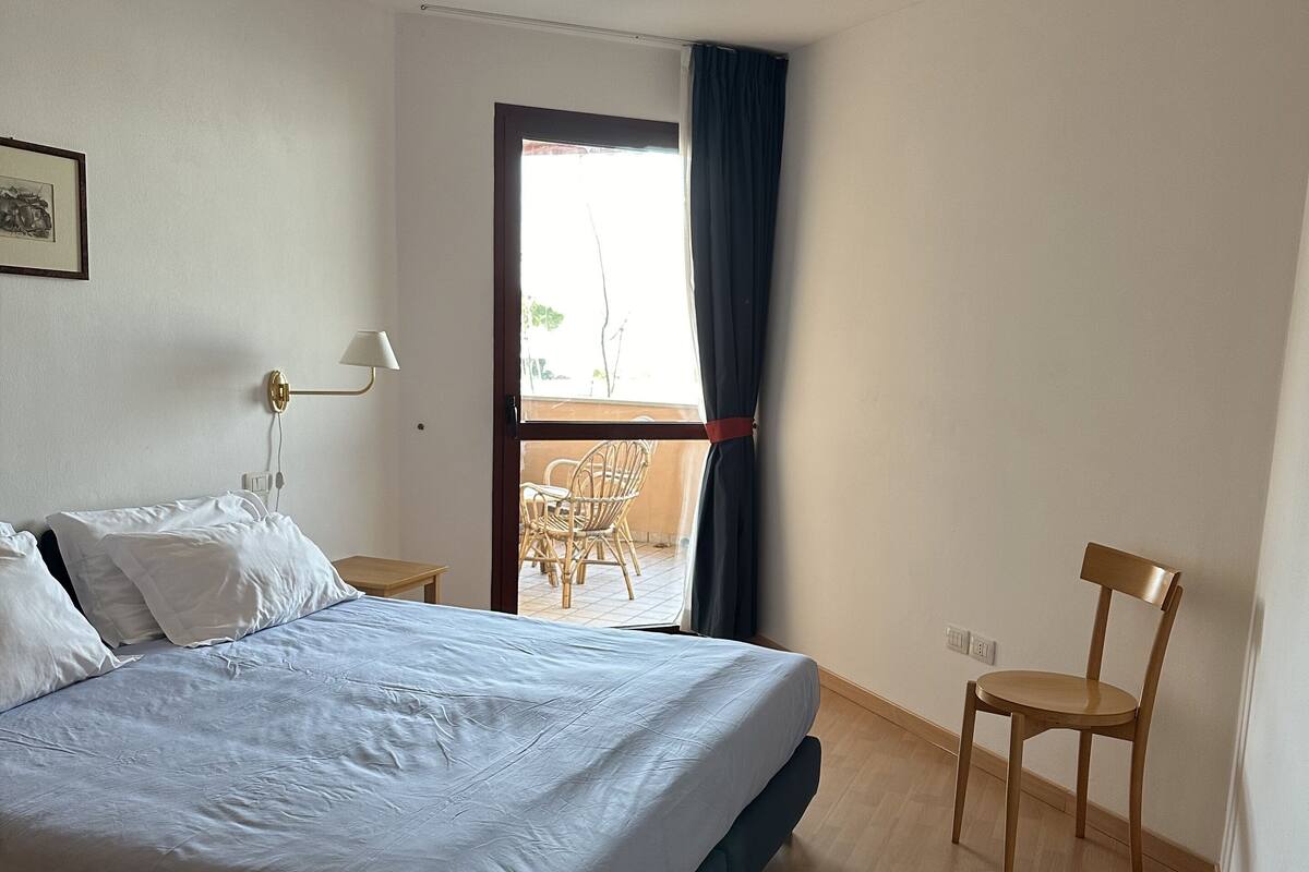 Une chambre d’hôtel avec un lit, une chaise, une table, une fenêtre avec des rideaux et une vue sur l’extérieur.