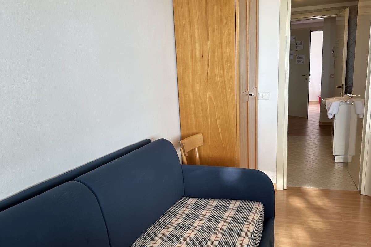 Une pièce avec un canapé bleu, une armoire en bois et une salle de bain visible à travers une porte ouverte.