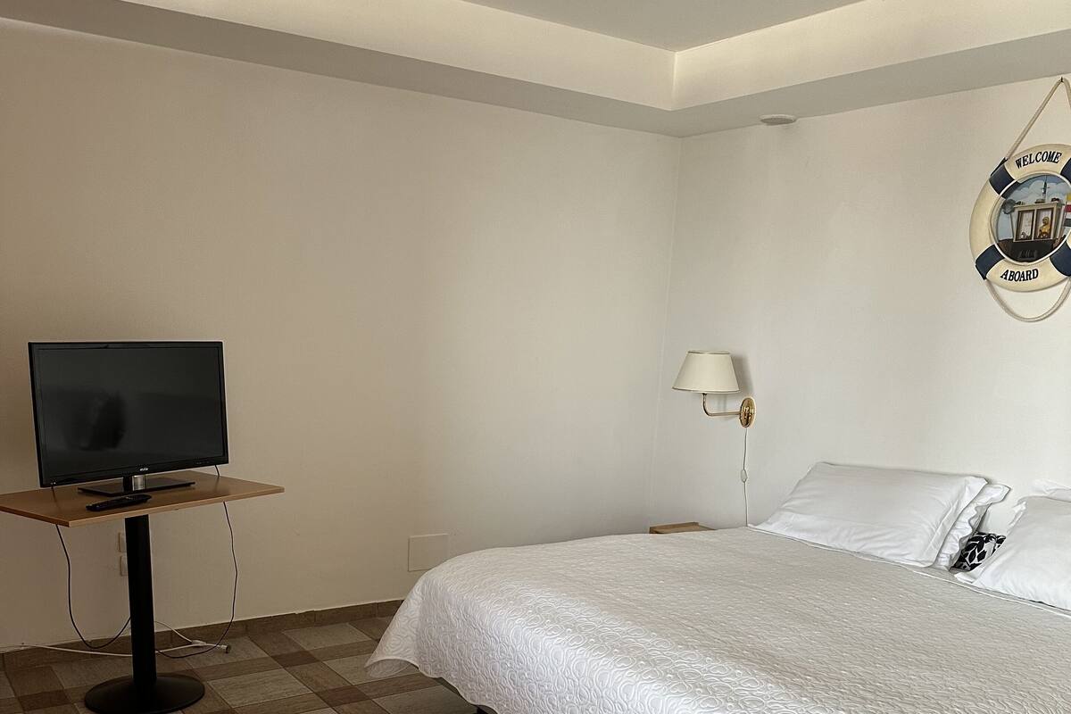 Une chambre d’hôtel avec un lit, un téléviseur posé sur un meuble, une lampe et un panneau d’accueil sur le mur.