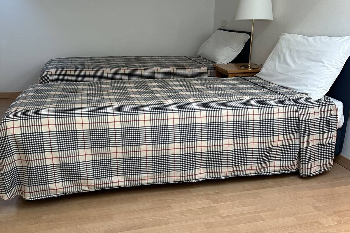 Une chambre avec deux lits, une table de chevet, une lampe et un mur blanc.