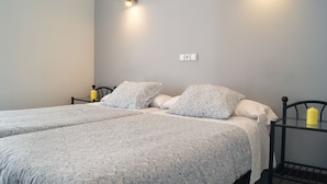 Una cama doble con ropa de cama estampada con motivos florales, una mesita de noche con una vela amarilla y una lámpara de pared.