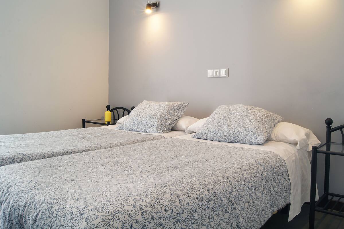 A double bed with floral-patterned bedding, a bedside table with a yellow candle, and a wall-mounted light fixture.