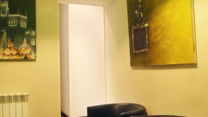 Una habitación con una lámpara de techo iluminada en verde, dos sillones negros, un cuadro y un radiador.