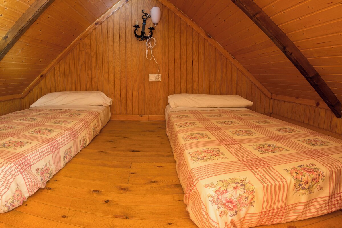 Um quarto de sótão pequeno e acolhedor, com duas camas simples, paredes de madeira e teto inclinado.