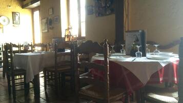 A dining area with multiple tables set for service, wooden chairs, and a tiled floor.