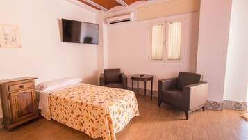 Un dormitorio con cama, televisión, silla, mesita y armario.