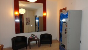 A room with two black armchairs, a small table with a decorative item, a large mirror with a wooden frame, and a vending machine. - Hostal Alistana (Madrid)
