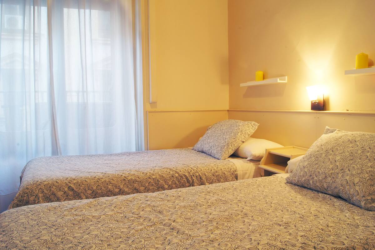 Une chambre d’hôtel avec deux lits, une table de chevet, une commode et une étagère murale avec des bougies.