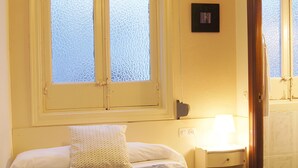 A bedroom with a bed, a window with frosted glass, a bedside table with a lamp, and a door. - Hostal Alistana (Madrid)