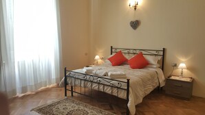 A neatly made bed with white linens, a patterned rug, and a bedside table with a lamp. - Garden Suite (Genoa)