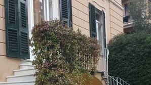 A set of white stone steps leading up to a building with green shutters and a small round table at the bottom. - Garden Suite (Genoa)