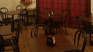 A dining area with wooden tables and chairs, a large arched red door, a chandelier, and a mirror on the wall. - Garden Suite (Genoa)
