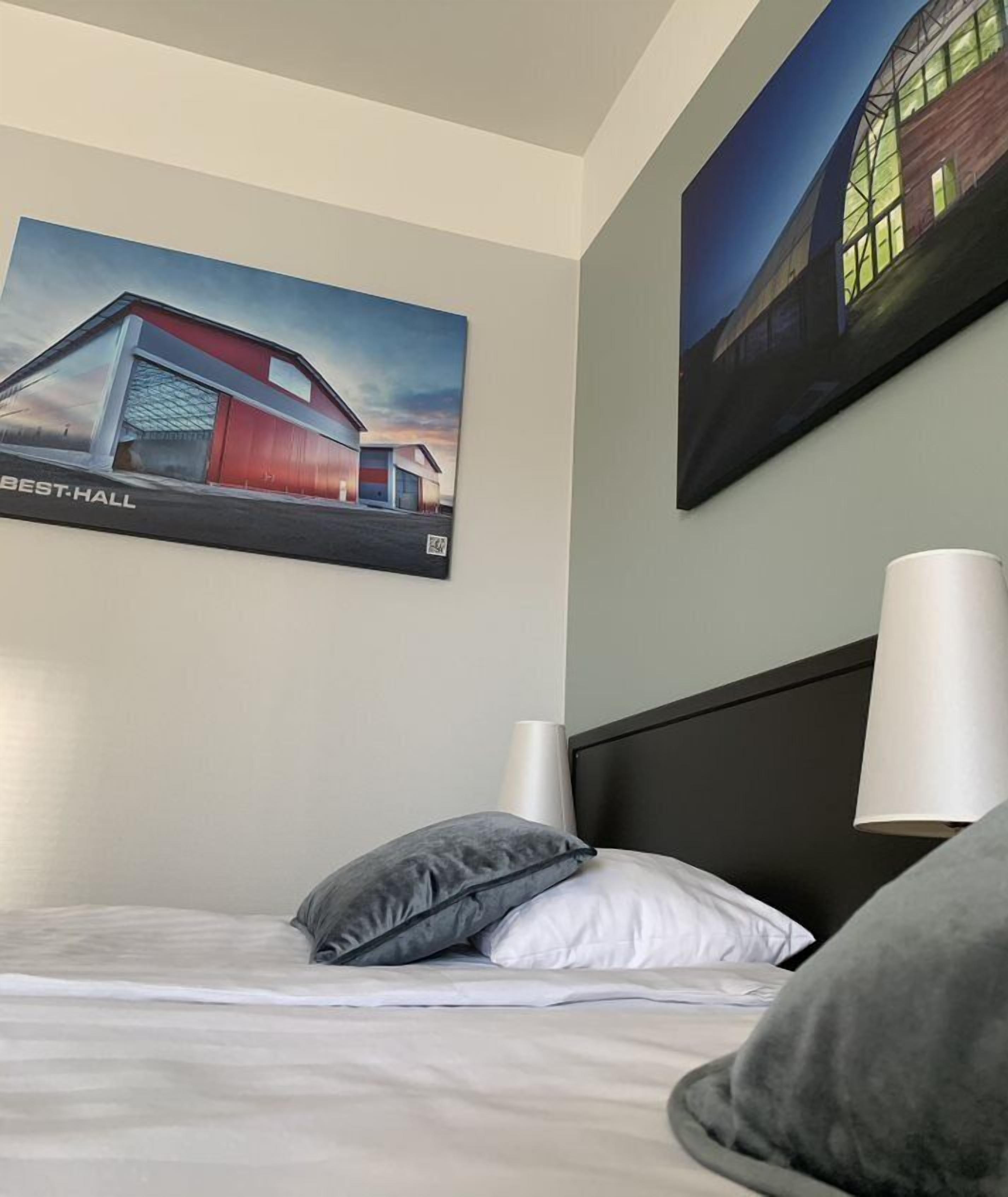 A hotel room with a bed, a nightstand, a lamp, and two paintings on the wall.