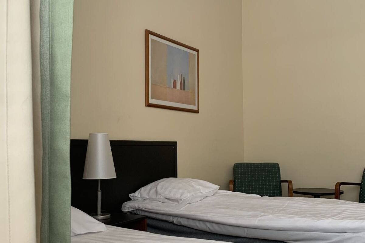 Une chambre d’hôtel avec deux lits, un bureau, une chaise, une lampe et un tableau encadré au mur.
